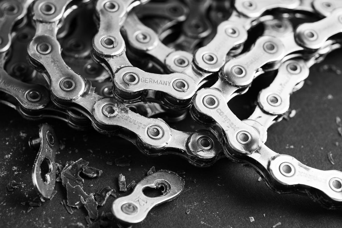 Nahaufnahme einer metallischen Fahrradkette mit dem eingravierten Wort GERMANY auf einem Glied, die auf einer dunklen Fläche mit Metallspänen in der Nähe liegt.