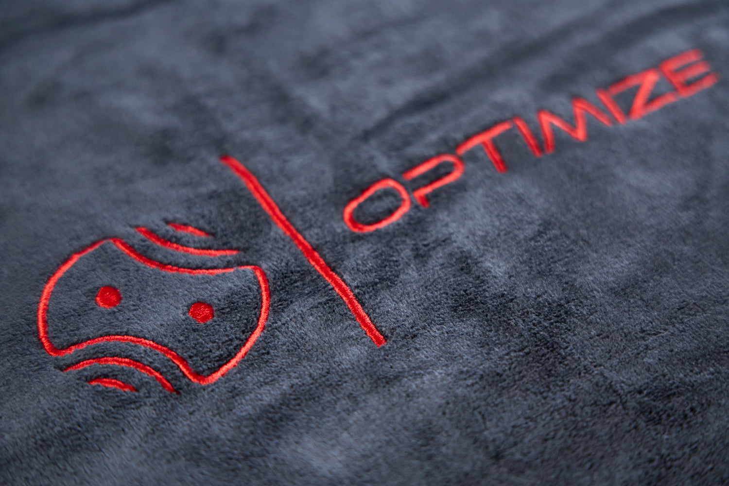 Nahaufnahme eines weichen, dunkelgrauen, fusselfreien Optimize Mikrofaser Reinigungstuches der Optimize GmbH mit aufgesticktem roten Logo und