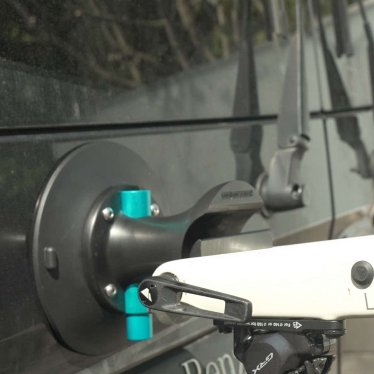Ein schwarzer Saugnapfhalter für Fahrräder, der an einer Fahrzeugscheibe befestigt ist und die Fahrradgabel an der Steckachse sichert.