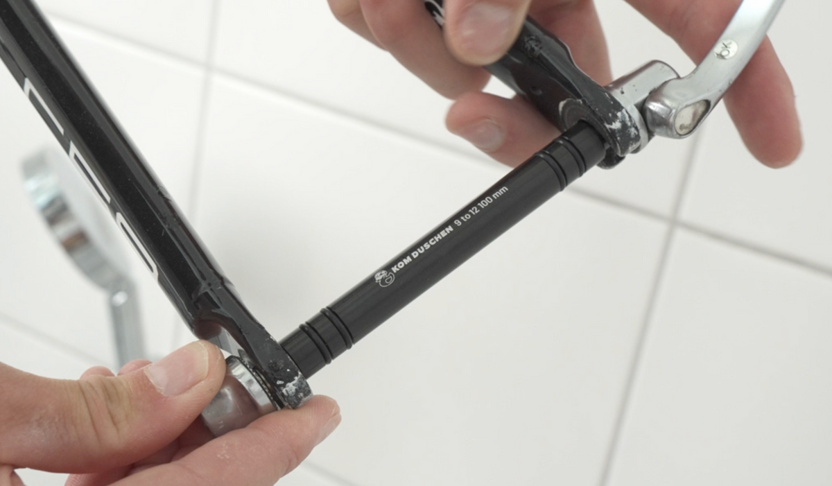 Hände, die einen schwarzen 12 x 100 mm Schnellspanner-Adapter in eine Fahrradgabel einsetzen.