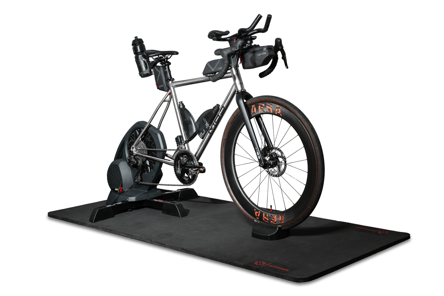 Ein silbernes Rennrad, das auf einem Smart-Trainer montiert ist, steht auf der „Optimize GmbH Indoor Matte“, die sich durch ein elegantes schwarzes Design auszeichnet. Das Fahrrad ist mit Trinkflaschen, Lenkertaschen und auffälligen orangefarbenen Reifenakzenten ausgestattet. Der Hintergrund ist schlicht weiß.