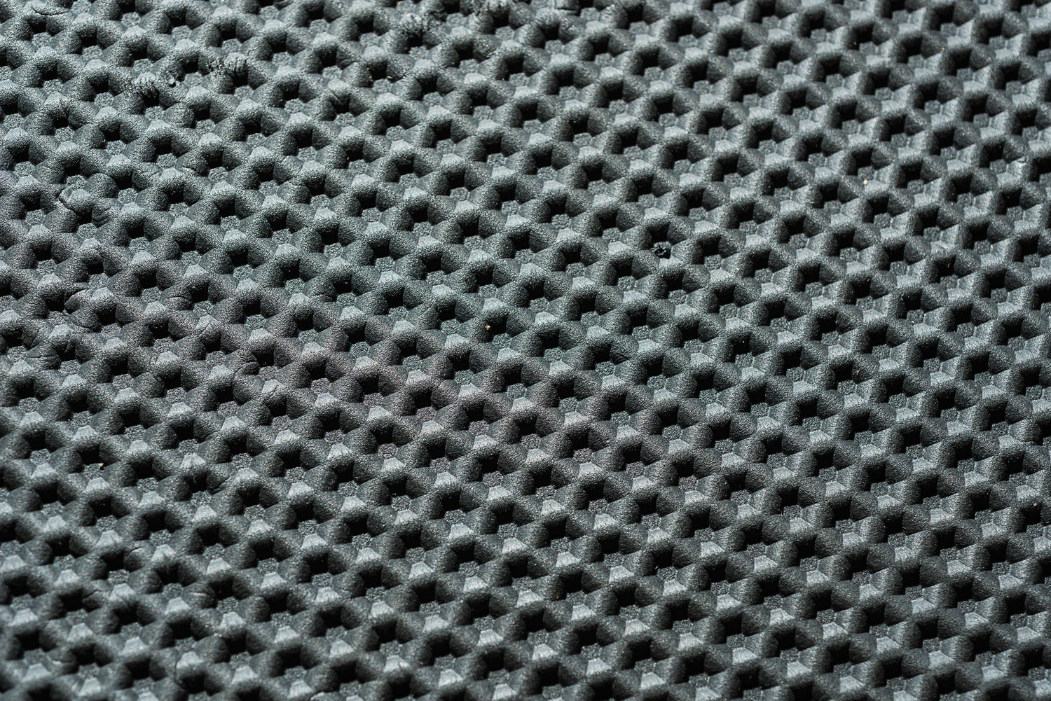 Nahaufnahme einer strukturierten schwarzen Oberfläche mit einem sich wiederholenden Muster aus kleinen, erhabenen sechseckigen Erhebungen und Vertiefungen – perfekt geeignet für die „Indoor Matte“ von Optimize GmbH. Die Beleuchtung unterstreicht den dreidimensionalen Effekt des Designs, wodurch sich die Matte ideal als Trainingsmatte oder als Teil Ihres Smart-Trainer-Setups eignet.