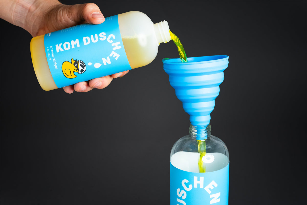 Eine Hand gießt gelbe Flüssigkeit aus einer Flasche durch einen blauen Silikon-Trichter in eine Glas-Sprühflasche, um Reinigungslösung umzufüllen.