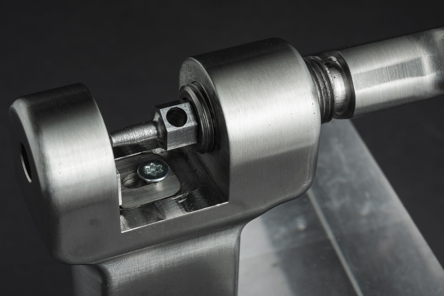 Nahaufnahme des „Optimize Kettennieter“ der Optimize GmbH, eines metallmechanischen Bauteils mit zylindrischen und sechseckigen Teilen, die präzise mittels CNC-Fräse bearbeitet wurden, sowie mit Montageelementen aus Edelstahl, montiert auf einem Metallsockel.