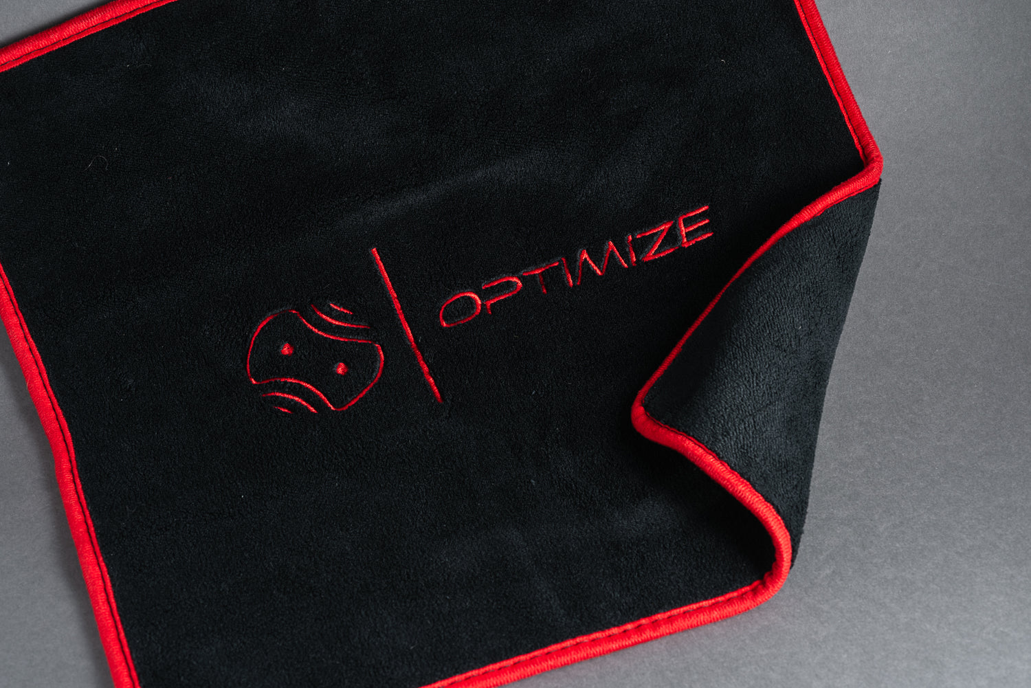 Das Optimize Premium Mikrofasertuch von Optimize GmbH mit rotem Rand, abstraktem Logo und rotem