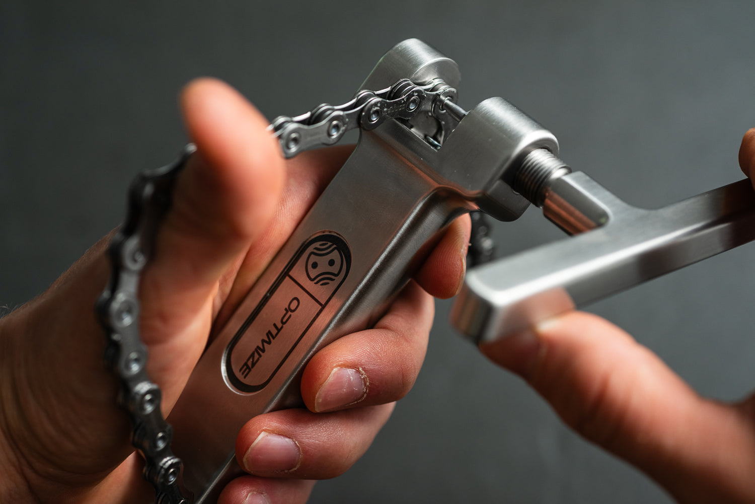 Nahaufnahme von Händen, die mit einem silbernen „Optimize Kettennieter“ einen Stift aus einer Fahrradkette herausdrücken, wobei das Logo der Optimize GmbH auf dem Werkzeug zu sehen ist, das mit der Präzision einer CNC-Fräse fachmännisch gefertigt wurde.
