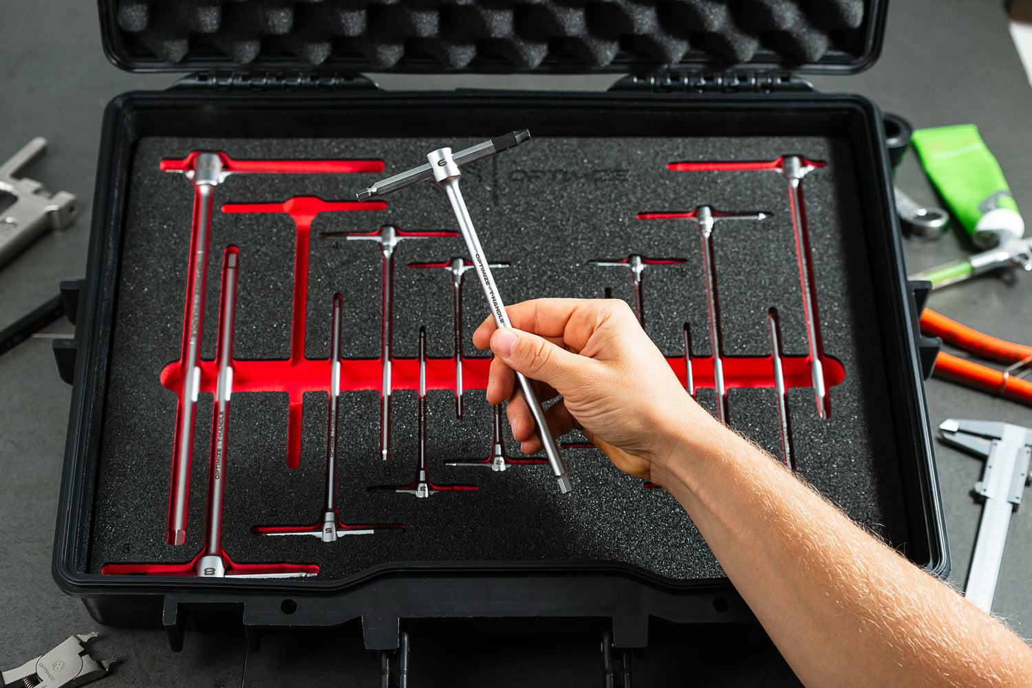 Eine Hand hält ein T-Griff-Bohrungsmessgerät über einem offenen Optimize Werkzeugkoffer der Optimize GmbH, in dem Präzisionsmesswerkzeuge übersichtlich in Schaumstoffausschnitten für ein effizientes Aufbewahrungssystem organisiert sind.
