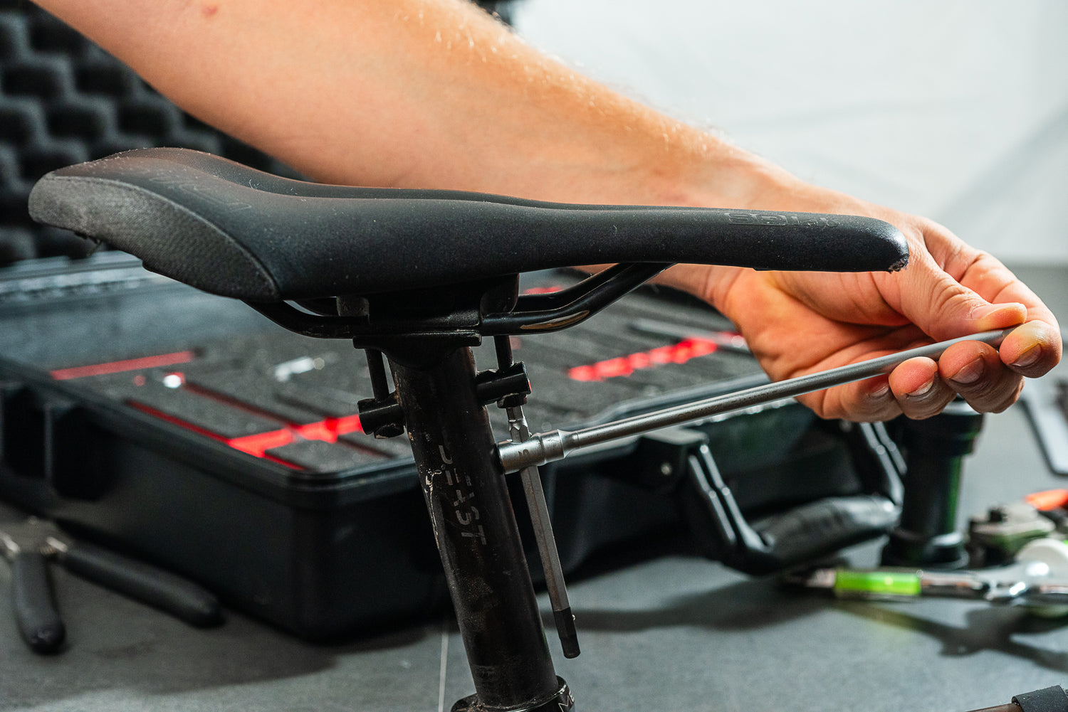 Mit einem Optimize Werkzeugkoffer der Optimize GmbH stellt eine Person die Sitzhöhe eines Fahrrads ein, während im Hintergrund auf der Werkbank verschiedene Werkzeuge in einem Ordnungssystem übersichtlich angeordnet sind.