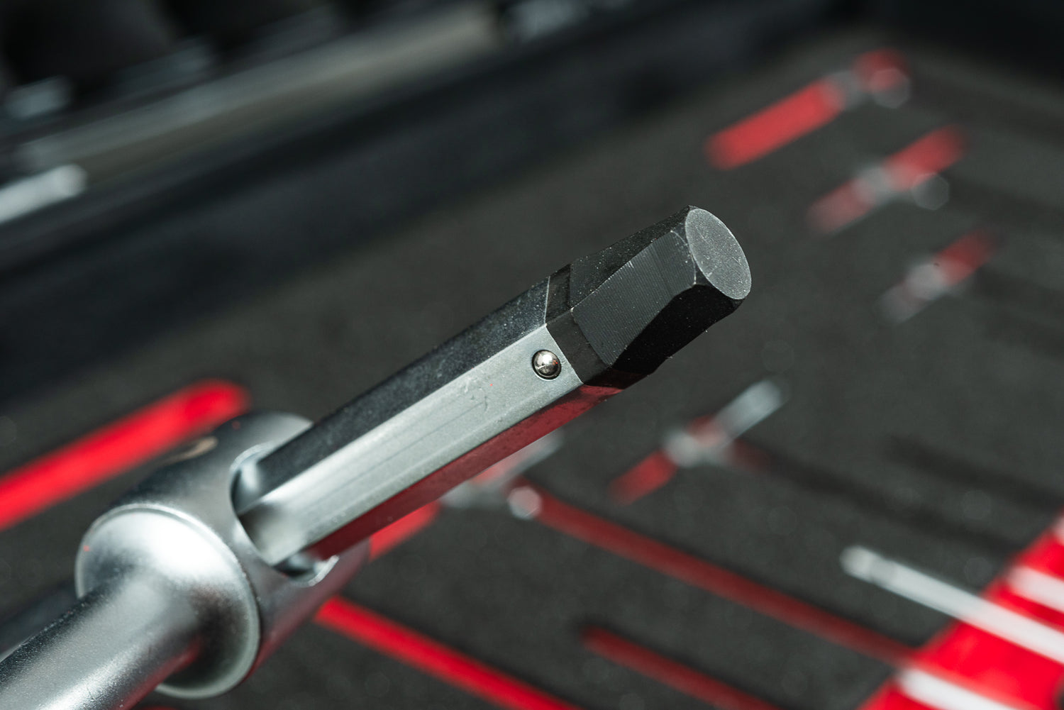 Nahaufnahme eines Innensechskant-Werkzeugs mit schwarzem Sechskant auf einer silbernen Ratsche, vor einem Optimize Werkzeugkoffer und rotem Ordnungssystem der Optimize GmbH, das für eine organisierte Werkzeugaufbewahrung konzipiert ist.