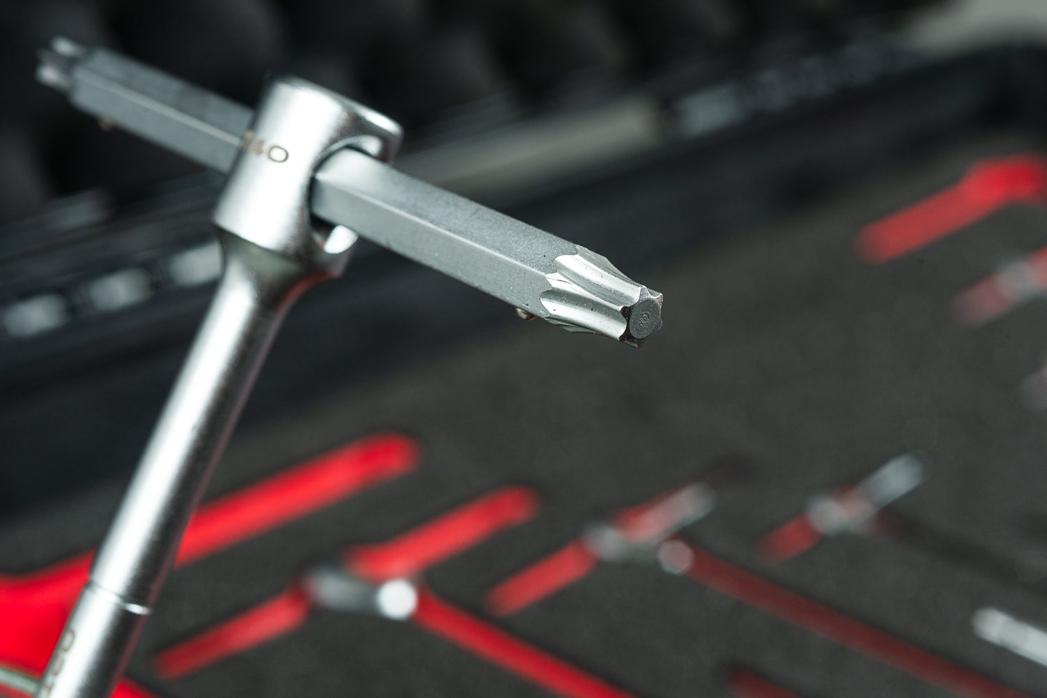 Ein silbernes T-Griff-Werkzeug mit sternförmigem Torx-Bit ist aus der Nähe zu sehen, im Hintergrund der Optimize Werkzeugkoffer der Optimize GmbH mit einem organisierten Schaumstoffeinsatz zur Aufbewahrung von zusätzlichem Fahrradwerkzeug.