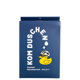 Eine blaue, rechteckige Produktverpackung für ein Mikrofasertuch – Premium 800 g/m² – mit der Abbildung einer Cartoon-Gummiente, die einen Fahrradhelm und eine Sonnenbrille trägt, sowie dem Text KOM DUSCHEN.