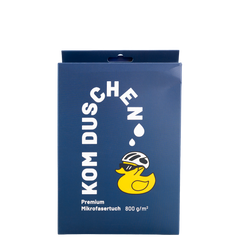 Eine blaue, rechteckige Produktverpackung für ein Mikrofasertuch – Premium 800 g/m² – mit der Abbildung einer Cartoon-Gummiente, die einen Fahrradhelm und eine Sonnenbrille trägt, sowie dem Text KOM DUSCHEN.