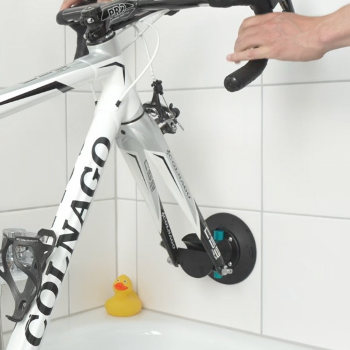Eine Fahrradgabel mit Steckachse, die mit einem großen schwarzen Saugnapfhalter KOM Duschen Saugnapfhalter Fahrrad an einer Badezimmerwandfliese befestigt ist.