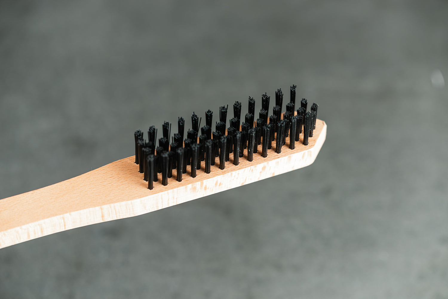 Eine Nahaufnahme der Optimize Kassetten-Reinigungsbürste von Optimize GmbH mit schwarzen Borsten, die schräg vor einem einfarbig grauen Hintergrund gezeigt wird - perfekt für alle, die ihre Kassette reinigen oder ihren Fahrradantrieb makellos halten wollen.