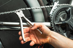 Eine Person verwendet die „Optimize Kettenschloss-Zange“, ein spezielles Fahrradkettenwerkzeug, das in Deutschland von der Optimize GmbH hergestellt wird, um Arbeiten an einer Kette im Bereich der Schaltung und der Kurbelgarnitur des Fahrrads durchzuführen.