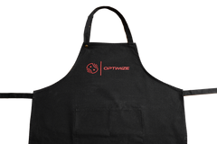 Die Optimize Heißwachsschürze von Mein Shop ist eine schwarze Baumwollschürze mit einem roten Logo und OPTIMIZE auf der Brust, ideal für Fahrradwerkstätten. Sie hat einen Nackenriemen, zwei seitliche Bänder, eine Fronttasche und ist auf weißem Grund.