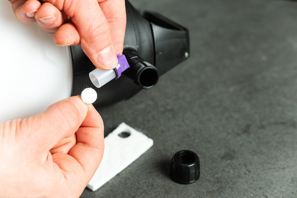 Hände, die einen kleinen runden Filter in die Düsenbaugruppe eines IK FOAM Pro 2 – Pumpsprüher-Schaumspenders zur Fahrradreinigung einsetzen.