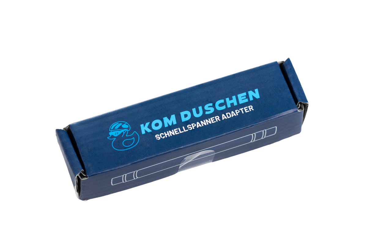 Blaue, rechteckige Schachtel für einen Schnellspanner-Adapter mit dem Entenlogo der KOM Duschen GmbH und der Aufschrift 12x100 mm Steckachsenaufnahme auf der Vorderseite.