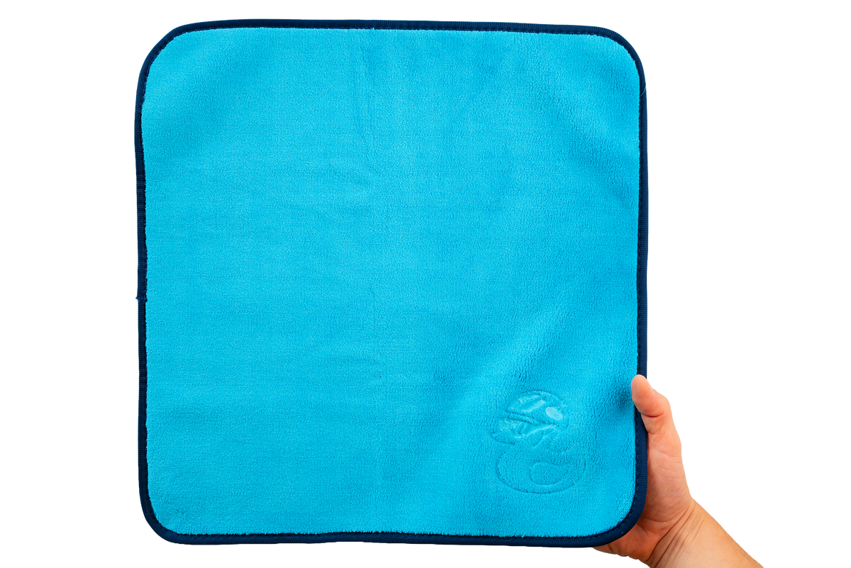 Eine Hand hält ein leuchtend blaues Mikrofasertuch – Premium 800 g/m² – mit einem dunkelblauen Rand und einem geprägten Entenlogo in der Ecke.