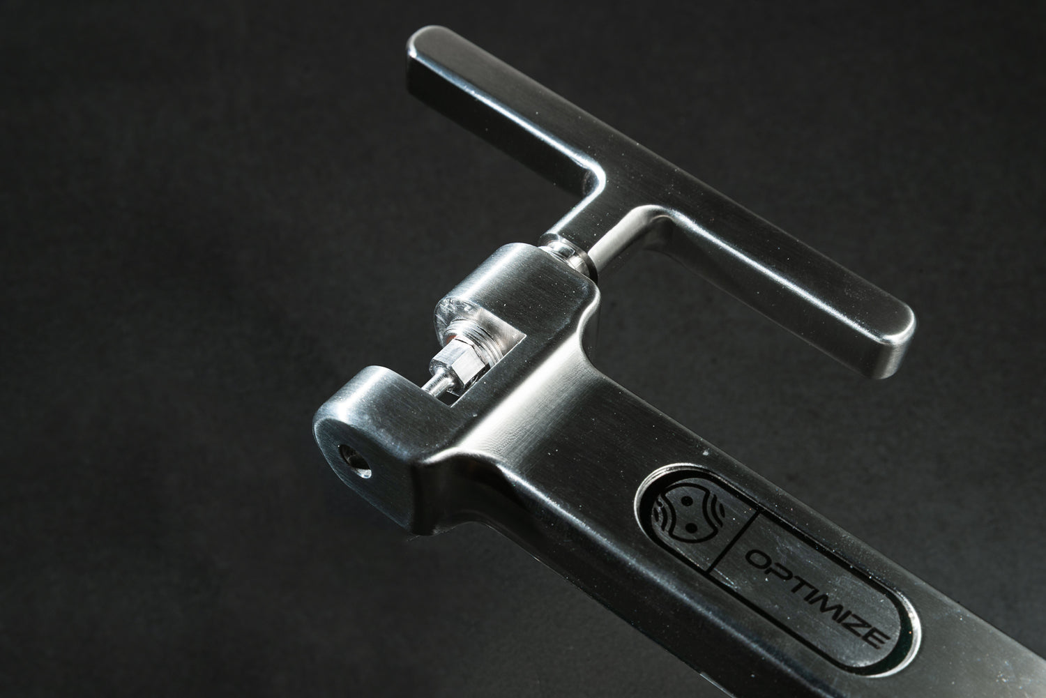 Eine Nahaufnahme des schlanken, metallischen Optimize-Kettennieters der Optimize GmbH, gefertigt aus hochwertigem Edelstahl, mit dem elegant in den Griff eingravierten Markennamen; vor einem dunklen Hintergrund bringen seine präzisen Konturen die CNC-Frästechnik zur Geltung – was ihn zu einem unverzichtbaren Kettennieter für Profis macht.