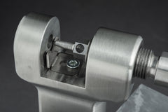 Eine Nahaufnahme des Kettennieters „Optimize Kettennieter“ der Optimize GmbH im Einsatz, bei der der Metallstift einen Kettengliedstift herausdrückt. Das aus Edelstahl gefertigte und mittels CNC-Fräse präzisionsbearbeitete Werkzeug hebt sich mit seiner silbernen Oberfläche deutlich vom sanft unscharfen grauen Hintergrund ab.