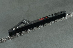 Die Optimize Kettenverschleißlehre der Optimize GmbH ist in schwarzer Farbe auf einer silbernen Shimano-, KMC- oder Connex-Fahrradkette über einer grauen Oberfläche abgebildet und zeigt Kettendehnungsmarkierungen zur präzisen Messung an.