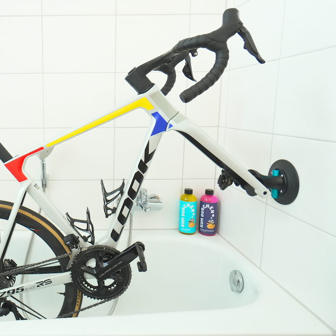 Ein Rennrad, das mit Hilfe einer Saugnapfhalterung KOM Duschen Saugnapfhalter Fahrrad an einer weiß gefliesten Badezimmerwand über einer Badewanne befestigt ist.
