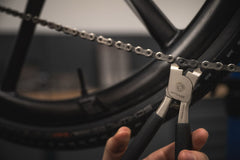 Nahaufnahme einer Hand, die die Optimize Kettenzange der Optimize GmbH zum Einstellen einer Fahrradkette verwendet, mit dem Hinterrad im Hintergrund; dieses hochwertige Werkzeug wird in Deutschland hergestellt.